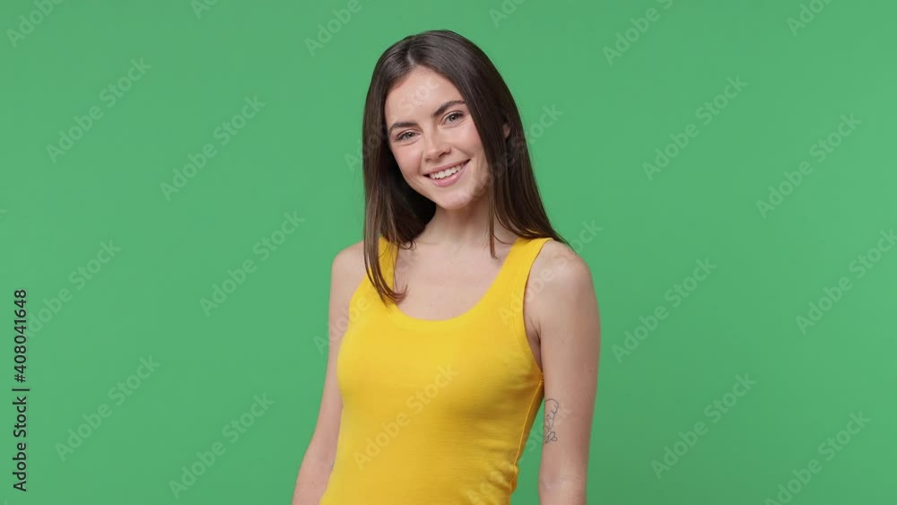 Smiling beautiful charming brunette young woman 20s years old in yellow casual tank top posing isolated on green color background in studio. People sincere emotions lifestyle concept. Looking camera Smiling beautiful charming brunette young woman 20s years old in yellow casual tank top posing isolated on green color background in studio. People sincere emotions lifestyle concept. Looking camera