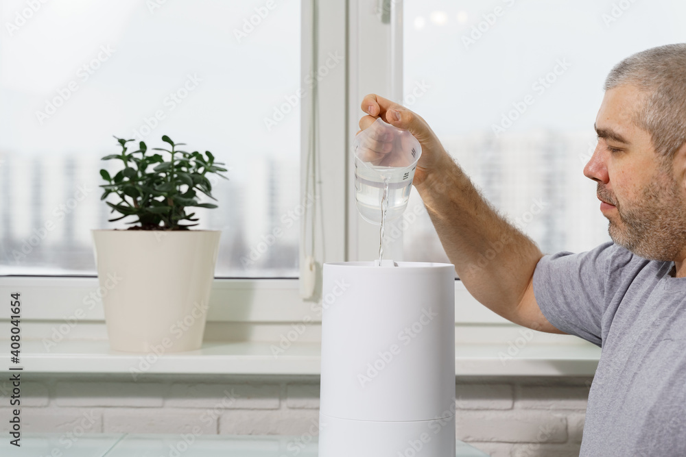 man pours water into a humidifier tank. using a humidifier at home