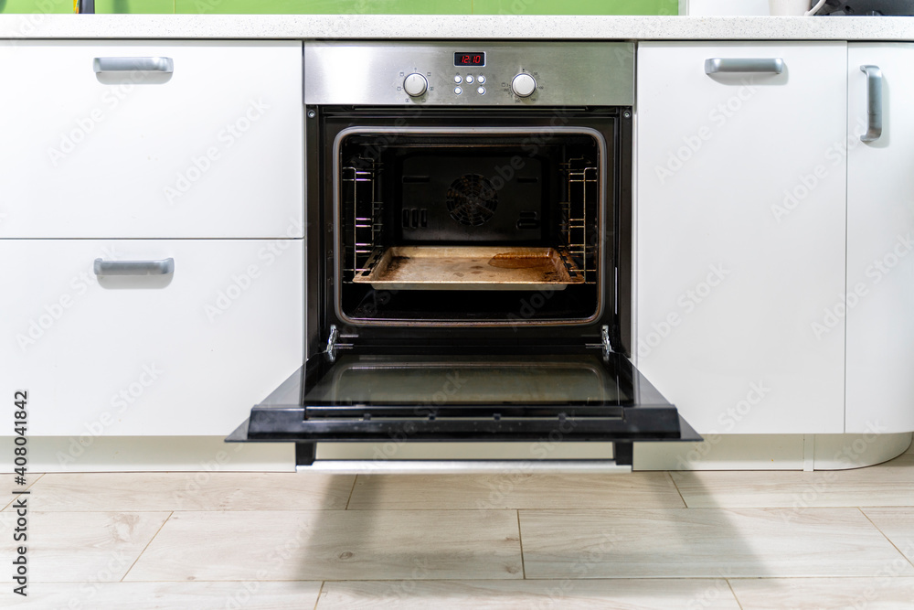 the door of a dirty oven is open in a bright kitchen. the door of a dirty oven is open in a bright kitchen.