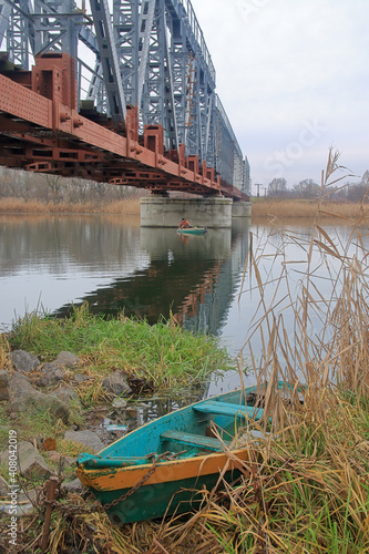 A fishing boat moored in the reeds under a railway bridge.