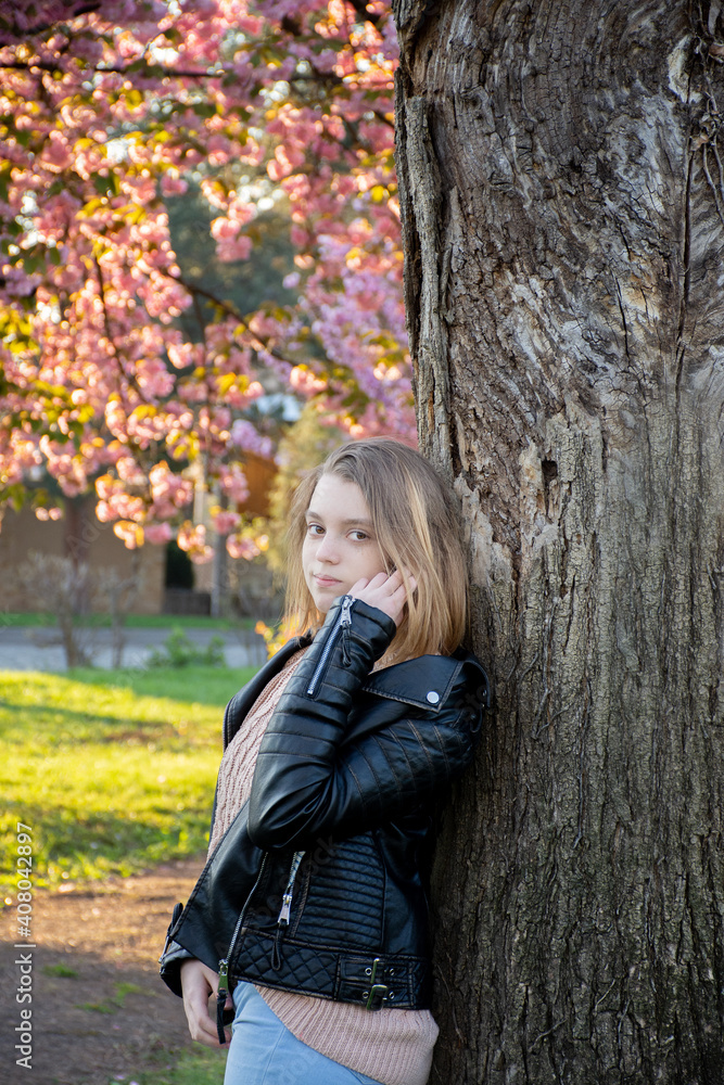 portrait of a young girl in a leather jacket on a background of flowering sakura trees portrait of a young girl in a leather jacket on a background of flowering sakura trees