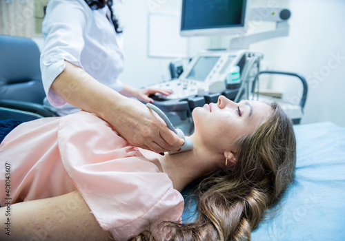 Doctor using ultrasound scanning machine for examining a thyroid of woman