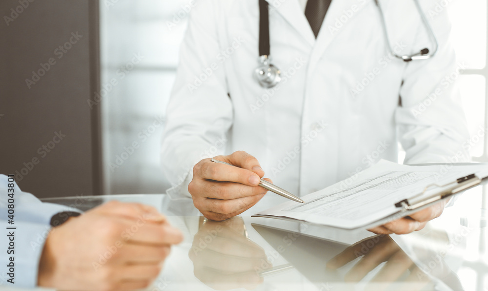 Unknown male doctor and woman-patient discussing current health examination while sitting in clinic and using clipboard. Good medical service in hospital. Medicine concept Unknown male doctor and woman-patient discussing current health examination while sitting in clinic and using clipboard. Good medical service in hospital. Medicine concept