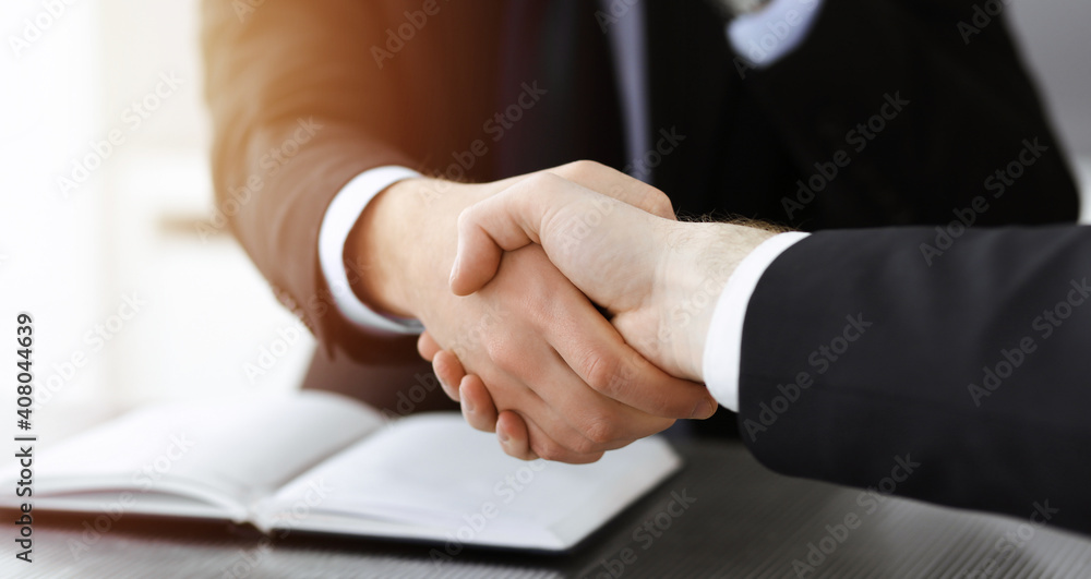 Businessman shaking hands with his colleague above the glass desk in sunny modern office, close-up. Unknown business people at meeting Businessman shaking hands with his colleague above the glass desk in sunny modern office, close-up. Unknown business people at meeting