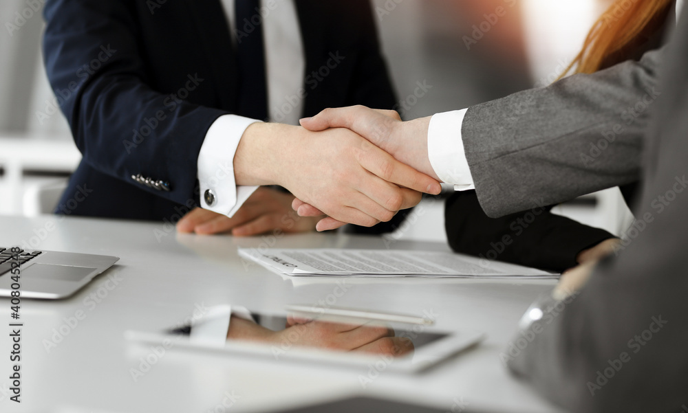 Unknown businessman shaking hands with his colleague or partner above the desk in sunny office, close-up Unknown businessman shaking hands with his colleague or partner above the desk in sunny office, close-up