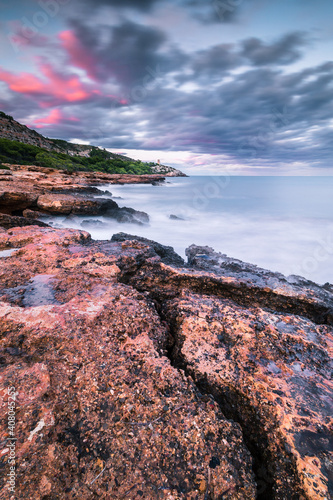 Larga exposición de un atardecer en una costa rocosa con rocas en primer plano y montañas verdes de fondo y cielo nuboso © Vicente Domingo