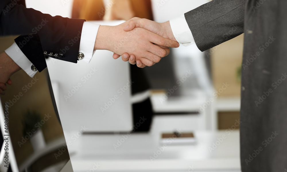 Unknown businessman shaking hands with his colleague or partner while standing straight in sunny office, close-up