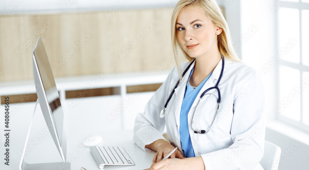 Portrate of woman-doctor at work while sitting at the desk in clinic. Blonde cheerful physician filling up medical form or prescription Portrate of woman-doctor at work while sitting at the desk in clinic. Blonde cheerful physician filling up medical form or prescription