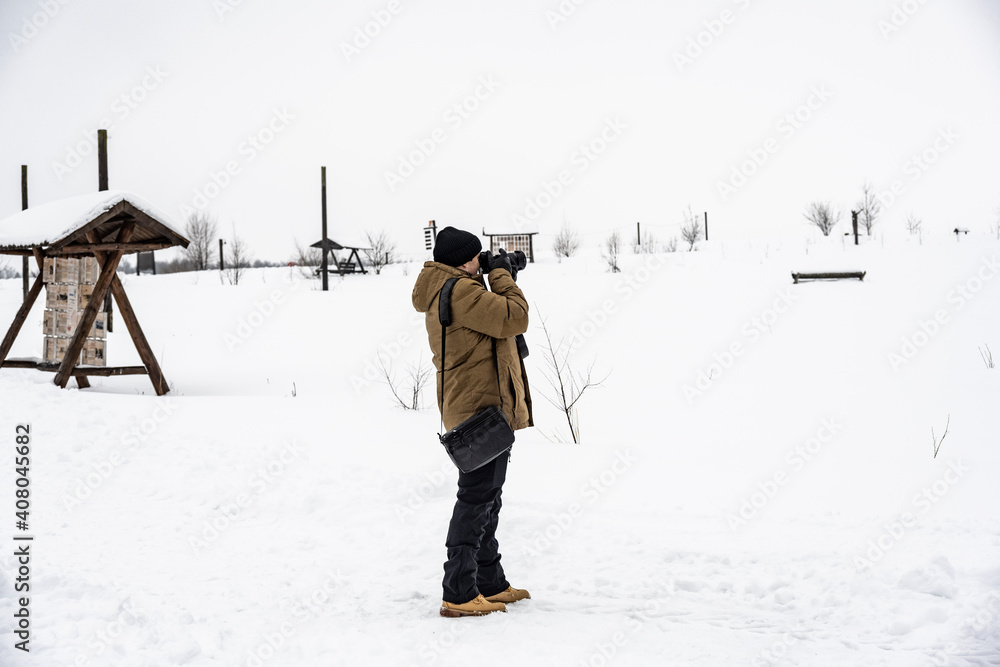 a man in a brown jacket photographs against a background of snow