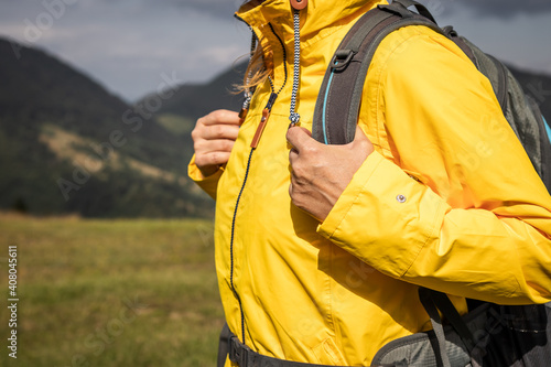 Sports clothing for extreme weather. Woman with backpack hiking in mountain and wearing yellow waterproof jacket photo
