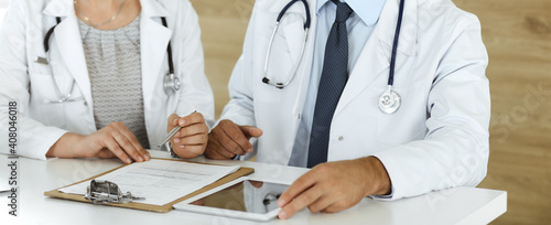 Two unknown doctors discussing treatment problems while sitting at the desk in hospital office, close-up. Data in medicine