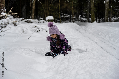 beautiful girl in a purple hat plays in the snow on a forest background