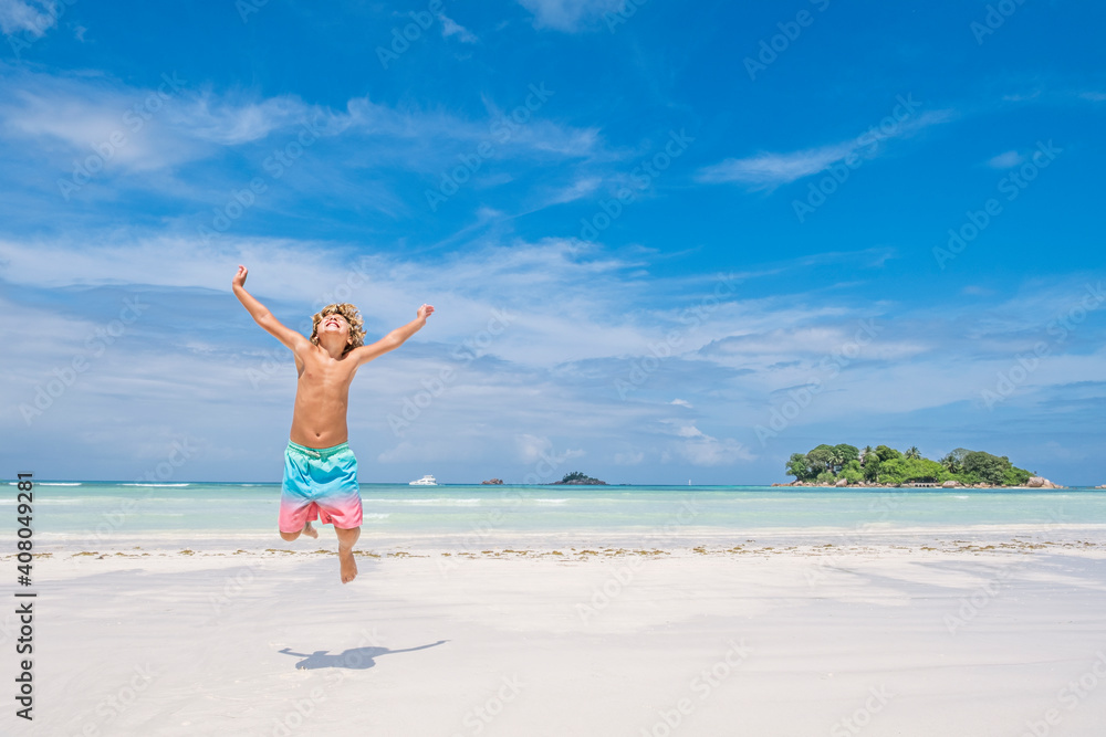 Young boy jumping of joy on tropical beach and island background, summer holiday concept Young boy jumping of joy on tropical beach and island background, summer holiday concept