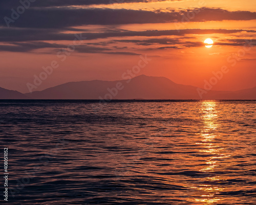 orange fiery sundown sky with some clouds over calm sea, dramatic nature background.