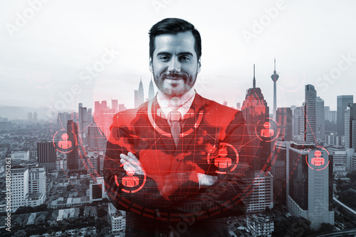 A young Caucasian HR director in cross hand pose is thinking about efficient strategy to recruit highly qualified specialists. Social media hologram icons over Kuala Lumpur background.