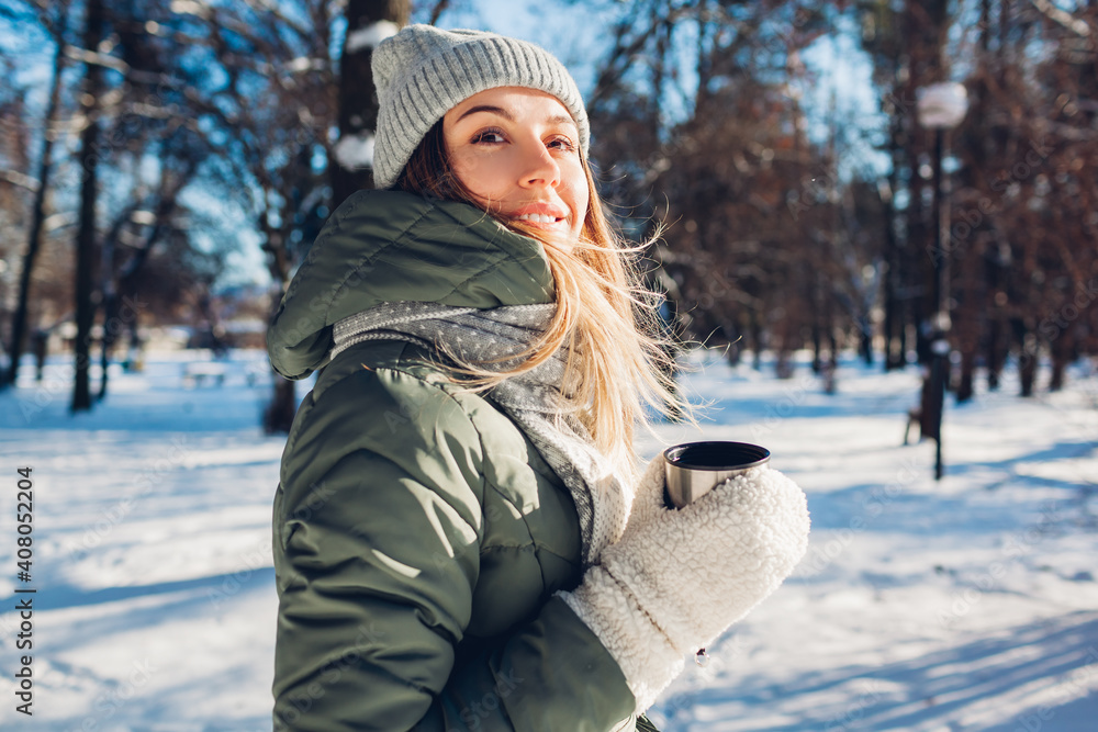 Woman drinking hot tea holding vacuum flask in winter park. Drinks to warm up in snowy frosty weather outdoors Woman drinking hot tea holding vacuum flask in winter park. Drinks to warm up in snowy frosty weather outdoors