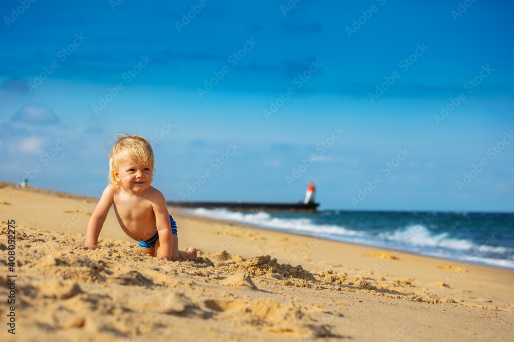 Happy little toddler boy crawl on the beach sand near the sea Happy little toddler boy crawl on the beach sand near the sea