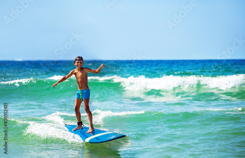 Little boy confidently ride waves on surfboard happy smiling and looking to camera
