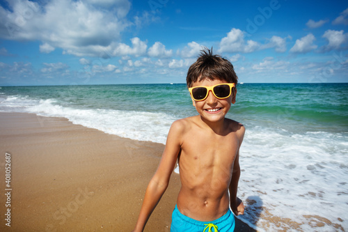 Portrait of a happy boy stand on the beach near the sea wear sunglasses and smile