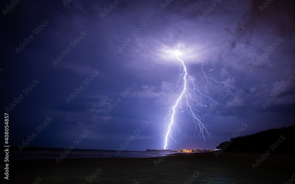 Lightening storm moving in over beach, with city. - obrazy, fototapety, plakaty 