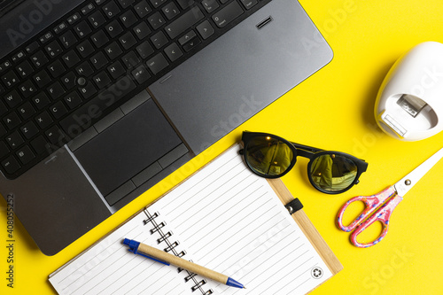 top view of workspace with laptop calculator note book sun glasses scissors and tape on yellow background. work concept. flat lay. photo