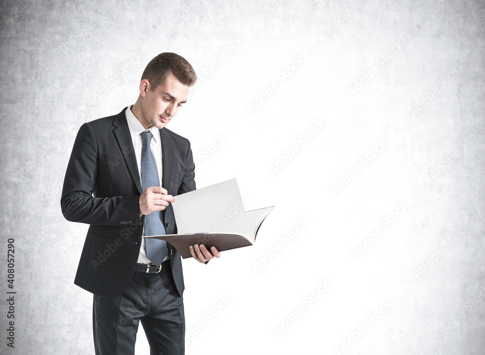 Young businessman reading document near concrete wall Young businessman reading document near concrete wall