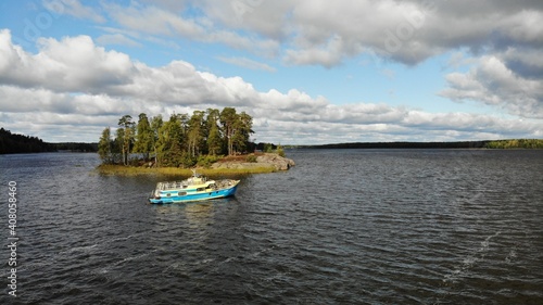 a boat is passing a small island. the view is from above. there are clouds in the sky and small waves.