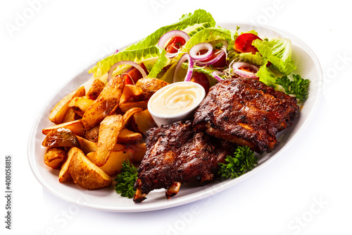 Tasty roasted ribs with baked potatoes vegetables on white background
