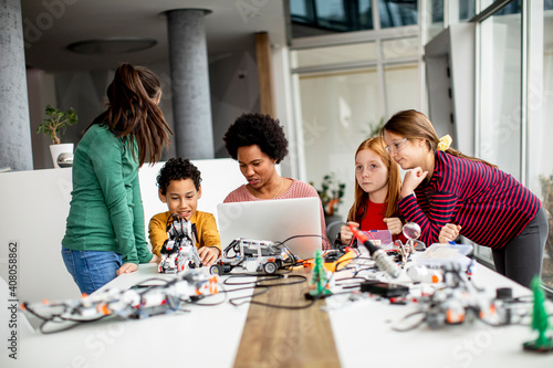 Happy kids with their African American female science teacher with laptop programming electric toys and robots at robotics classroom