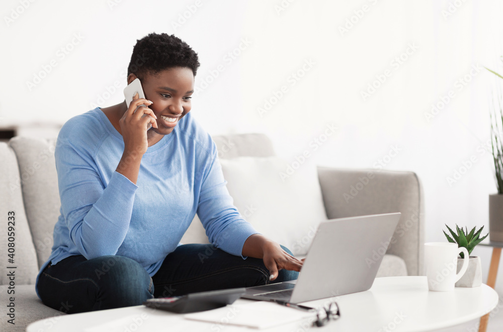 Young black woman talking on smartphone using laptop Young black woman talking on smartphone using laptop