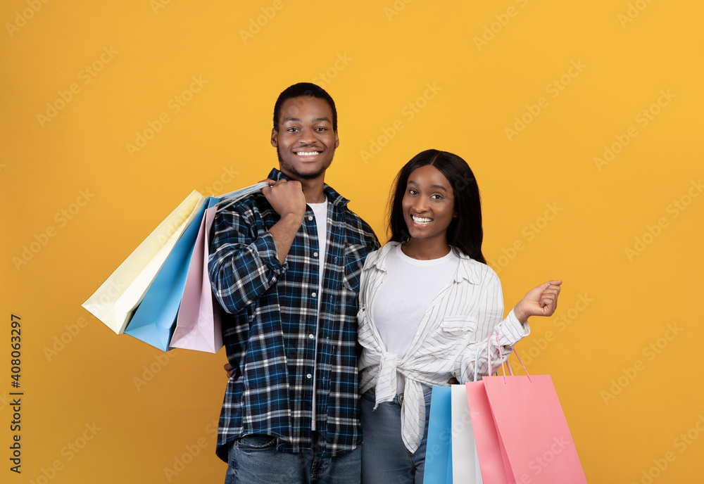 Smiling millennial african american husband and wife hold many colored packages with purchases after shopping Smiling millennial african american husband and wife hold many colored packages with purchases after shopping