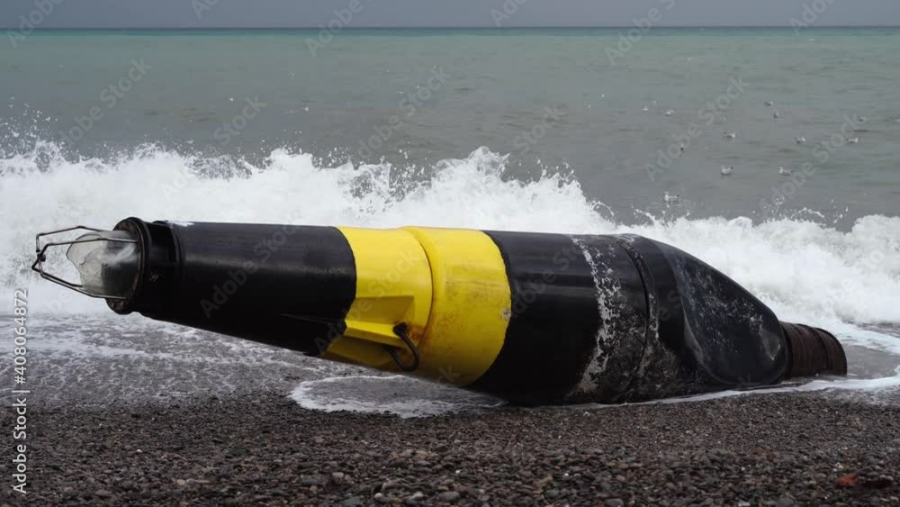 A large black and yellow buoy washed ashore after a storm. A broken sea