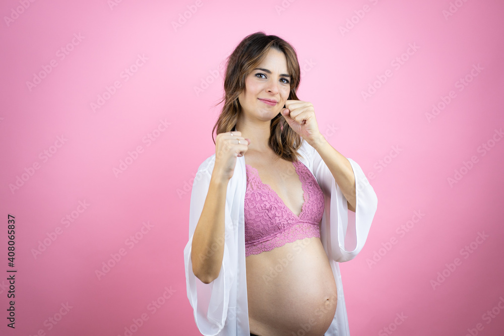 Young beautiful brunette woman pregnant expecting baby over isolated pink background Punching fist to fight, aggressive and angry attack, threat and violence