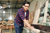 Concentrated mature carpenter in plaid shirt sawing long wooden plank in two pieces