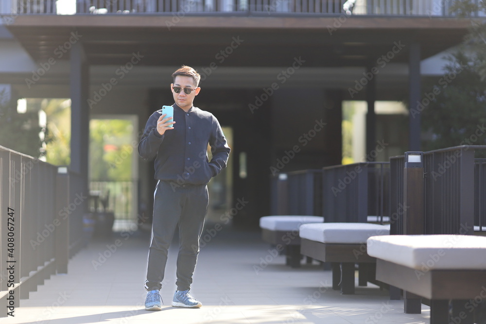 Fototapeta premium Asian man wearing training cloth for exercise is checking mobile phone for social media in the morning at residential house with copy space