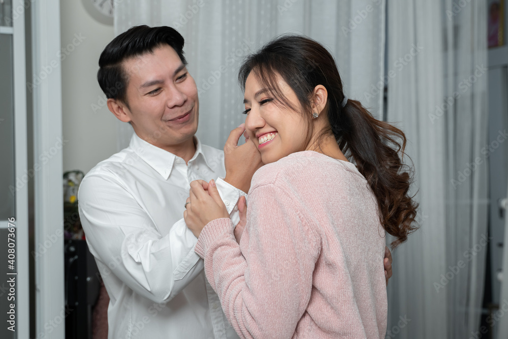 Asian young businessman wearing white long sleeves shirt looking at his wife while helping with buttoning up sleeves and she put her cheek on his hand. Family relationship concept Asian young businessman wearing white long sleeves shirt looking at his wife while helping with buttoning up sleeves and she put her cheek on his hand. Family relationship concept