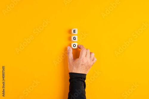 Photo Male hand placing the wooden blocks with the word Ego on yellow background