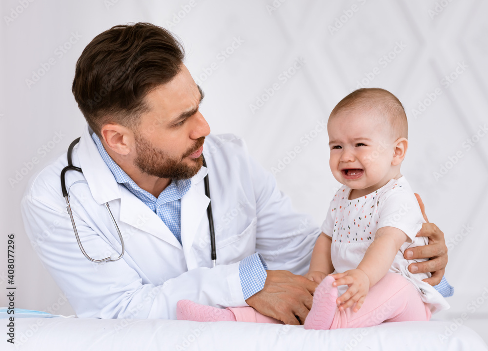 Baby Crying On Medical Checkup With Doctor Sitting In Clinic Baby Crying On Medical Checkup With Doctor Sitting In Clinic
