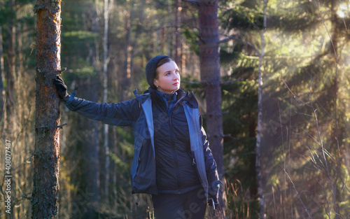 Happy woman hiker leaned against a tree in a sunny forest