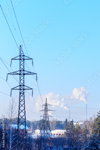 Power transmission towers in the foreground and a power plant in the background against a blue sky