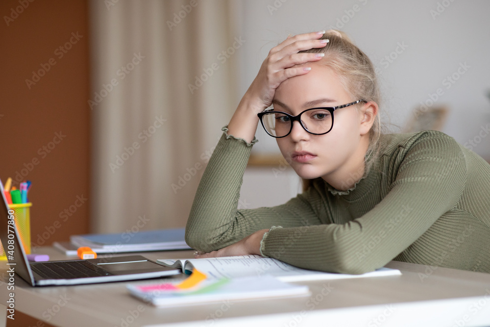 Bored teen girl sitting at home with book, doing homework Bored teen girl sitting at home with book, doing homework