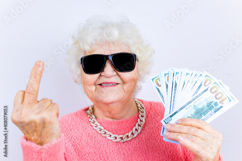 blonde old lady wear pinl sweater and sunglasses showing money isolated white background she is showing middle finger