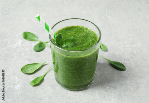 Green juice and fresh spinach leaves on light grey table