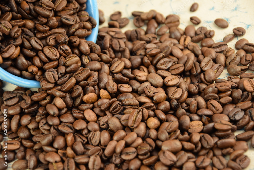 Fototapeta premium Coffee beans pouring out of a blue bowl Roasted Arabica grain coffee background
