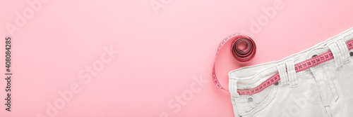Fotografie Measure tape with white jeans on light pink table background