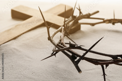 Crown of thorns and wooden cross on sand  closeup. Easter attributes