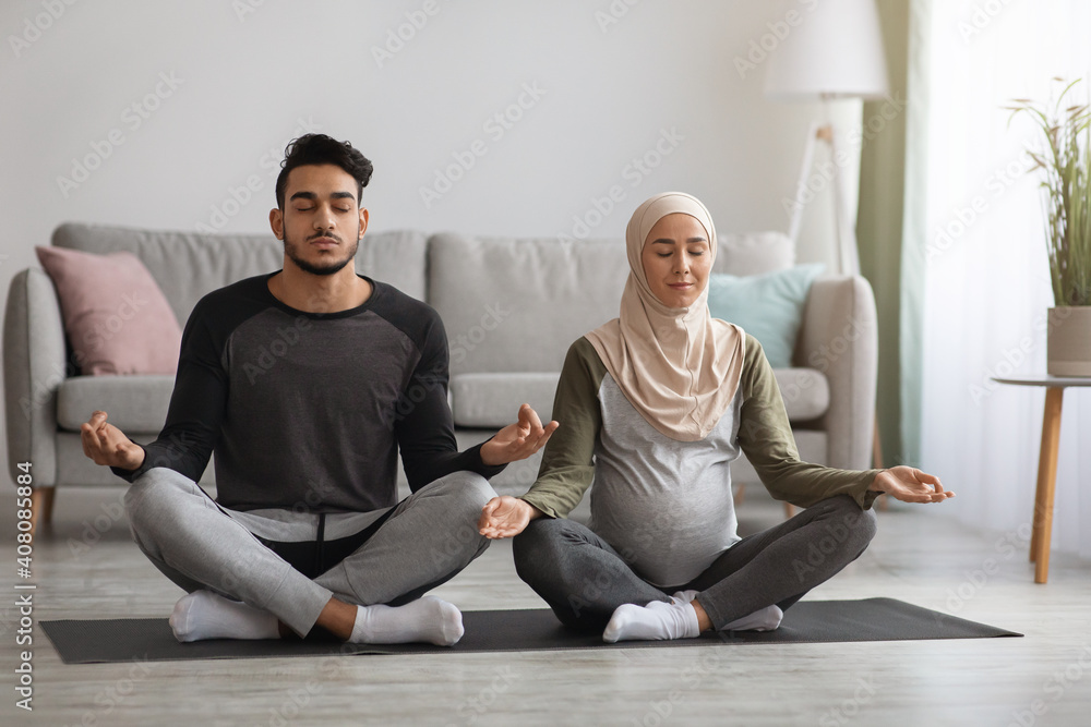 Prenatal Yoga Concept. Pregnant religious muslim couple meditating together at home - obrazy, fototapety, plakaty 