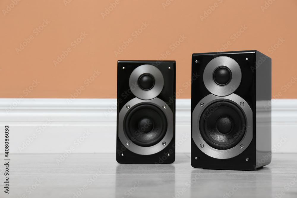 Modern powerful audio speakers on floor near orange wall Modern powerful audio speakers on floor near orange wall