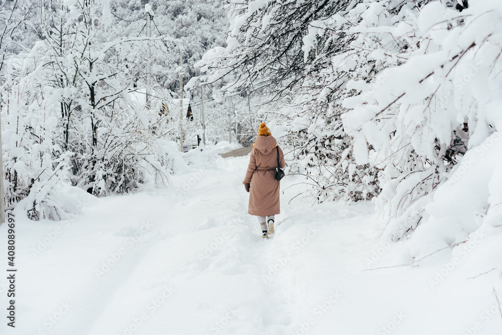 Back view of a woman in a coat and a yellow shake walking along a snowy path.
