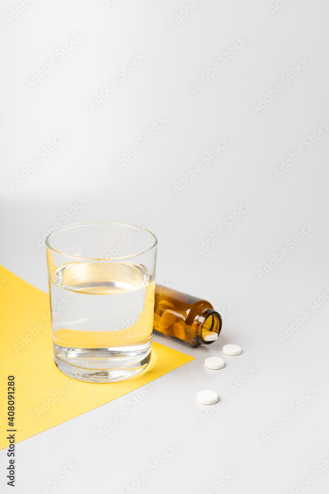 Glass of water and pills from a jar on white and yellow backgrounds